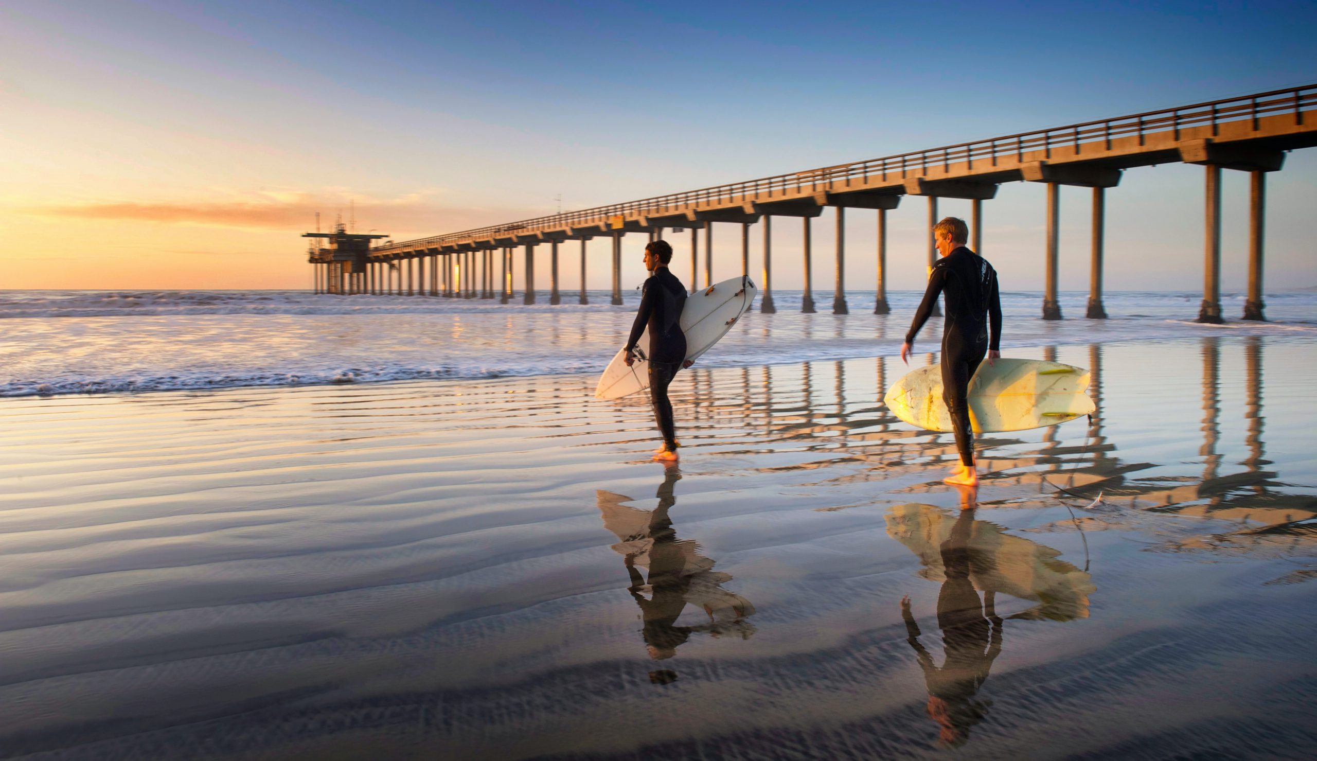 water Two surfers walking into the water by the peir | CoencE Web Development and Marketing